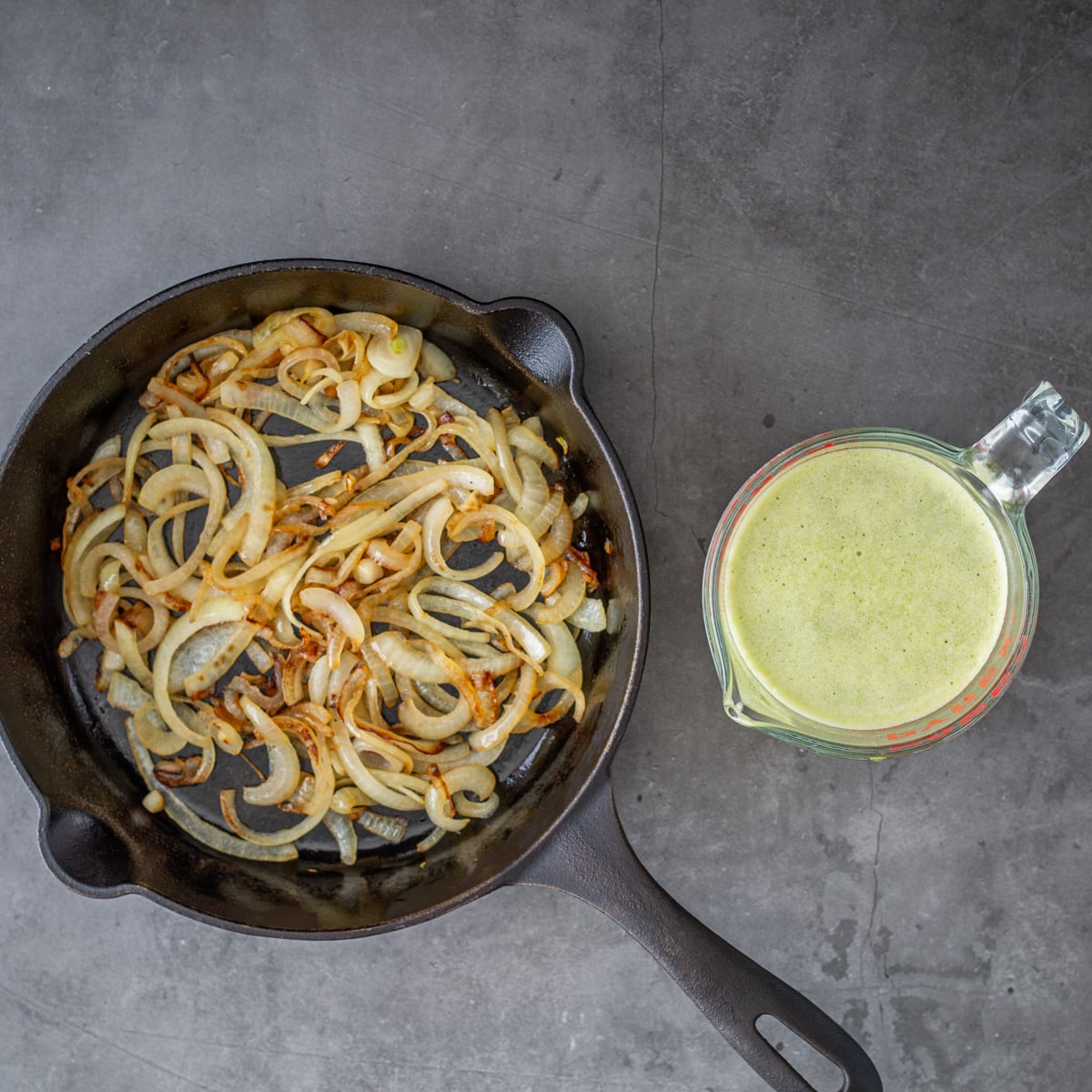 The onions are caramelized in a cast iron skillet, and the poblano cream sauce is in a glass pitcher.