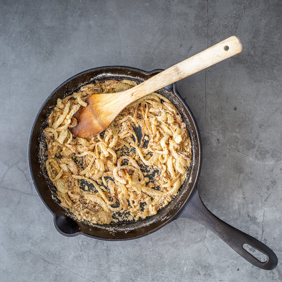 Masa, cumin, and garlic are added to the cast iron skillet with a wooden spoon.
