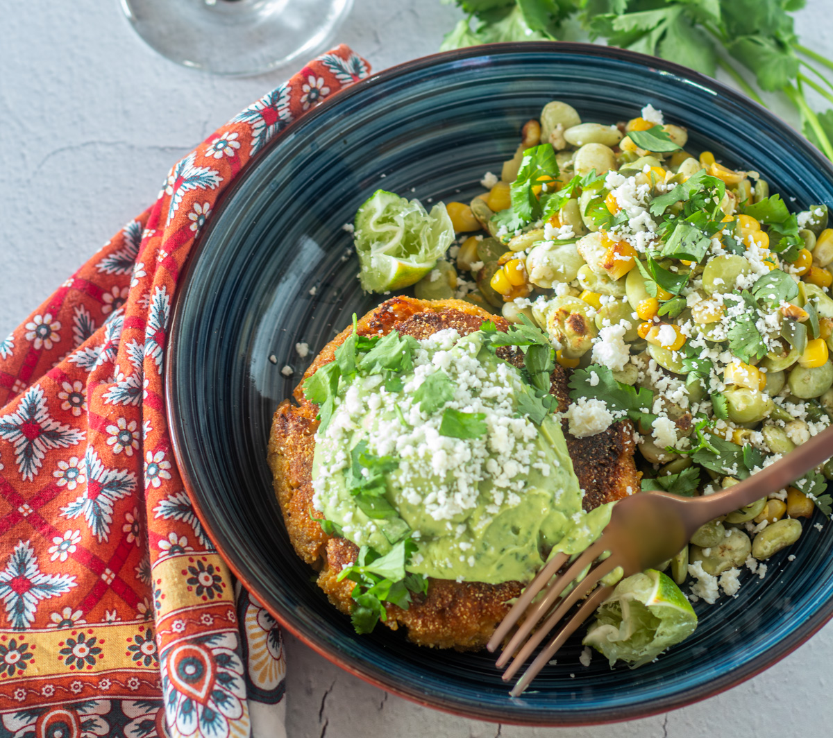 A close up of a Hatch chile salmon cake with Mexican street corn on a blue plate with cloth napkin.