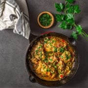 A cast iron skillet with the completed chicken thighs in blood orange juice with peppers and olives.