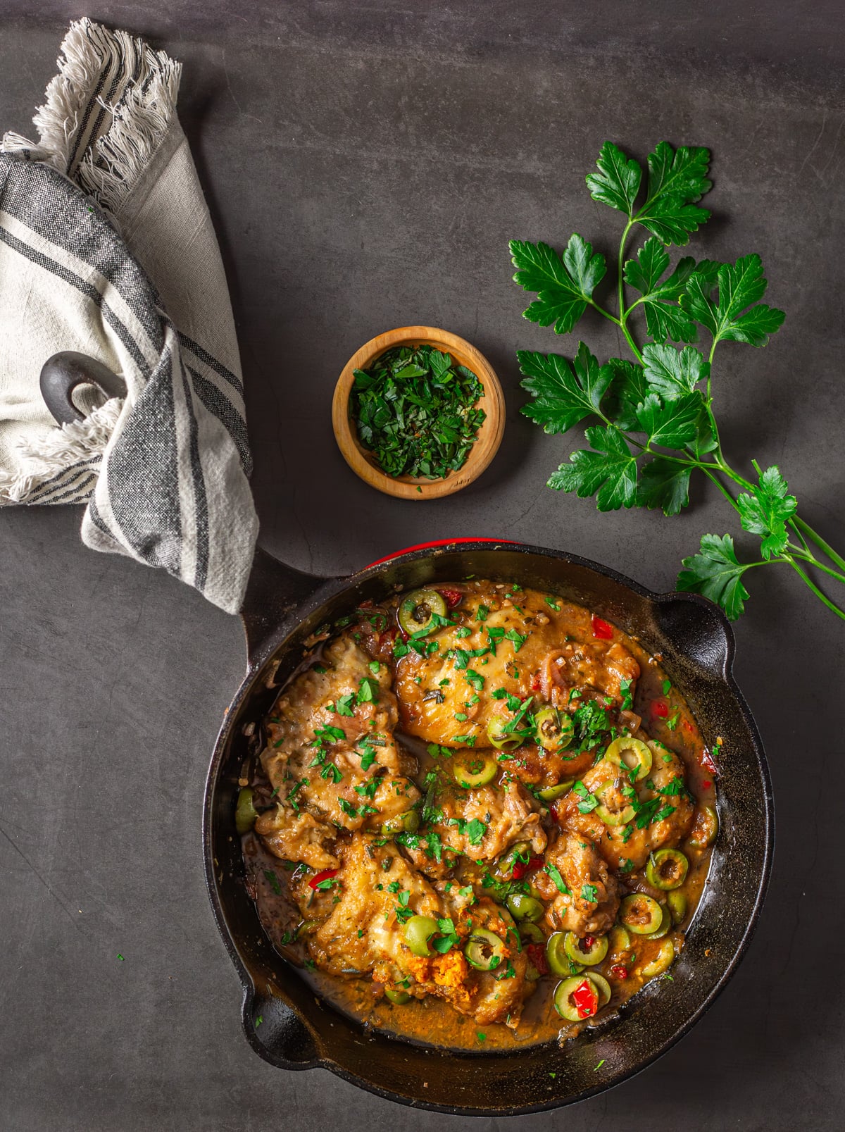 A cast iron skillet with Mediterranean blood orange chicken, fresh herbs, and cloth napkin.
