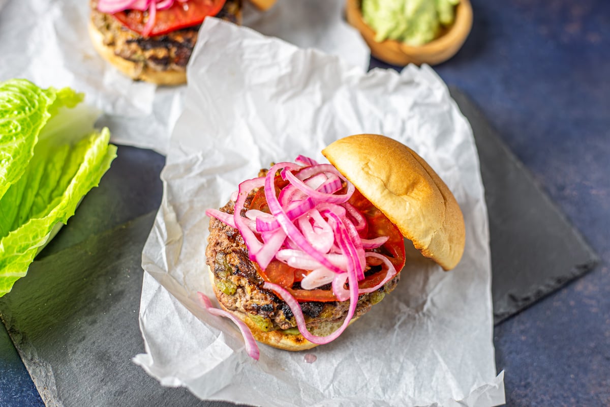 A piece of parchment with a beautiful Mexican burger, grilled bun, and toppings.