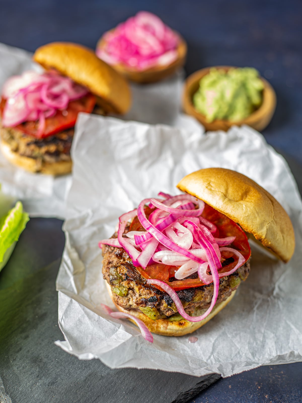 Two healthy Mexican burgers topped with quick pickled onions, smashed avocado, and tomato.