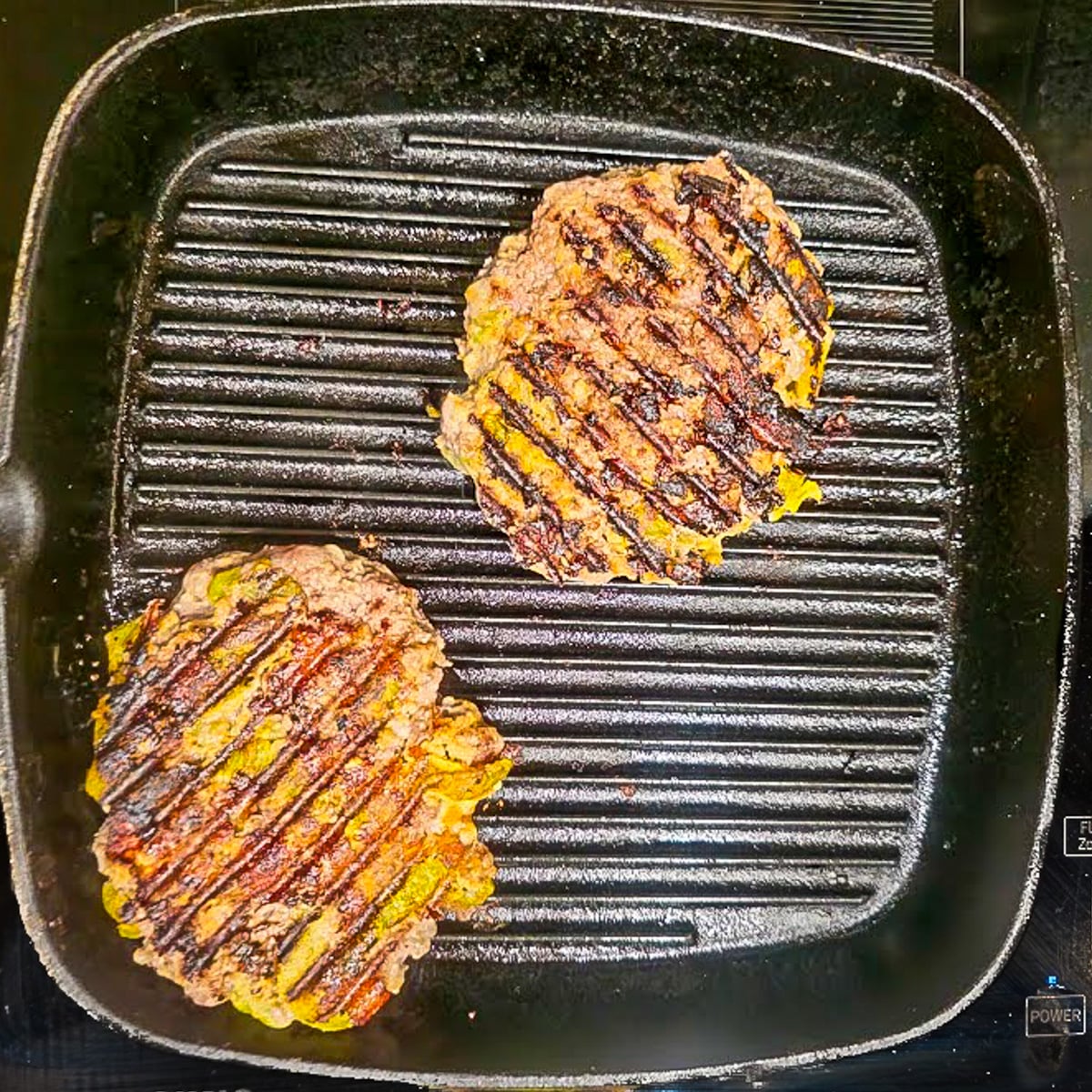 A stove top cast iron grill with 2 Mexican burger patties.