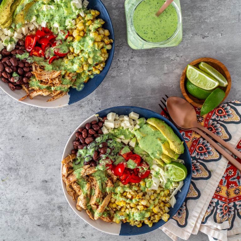 2 healthy taco bowls with bright napkin, copper flatware, and cilantro ranch dressing.