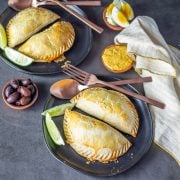 Two black ceramic plates with 2 beef/bison empanadas with garnishes.