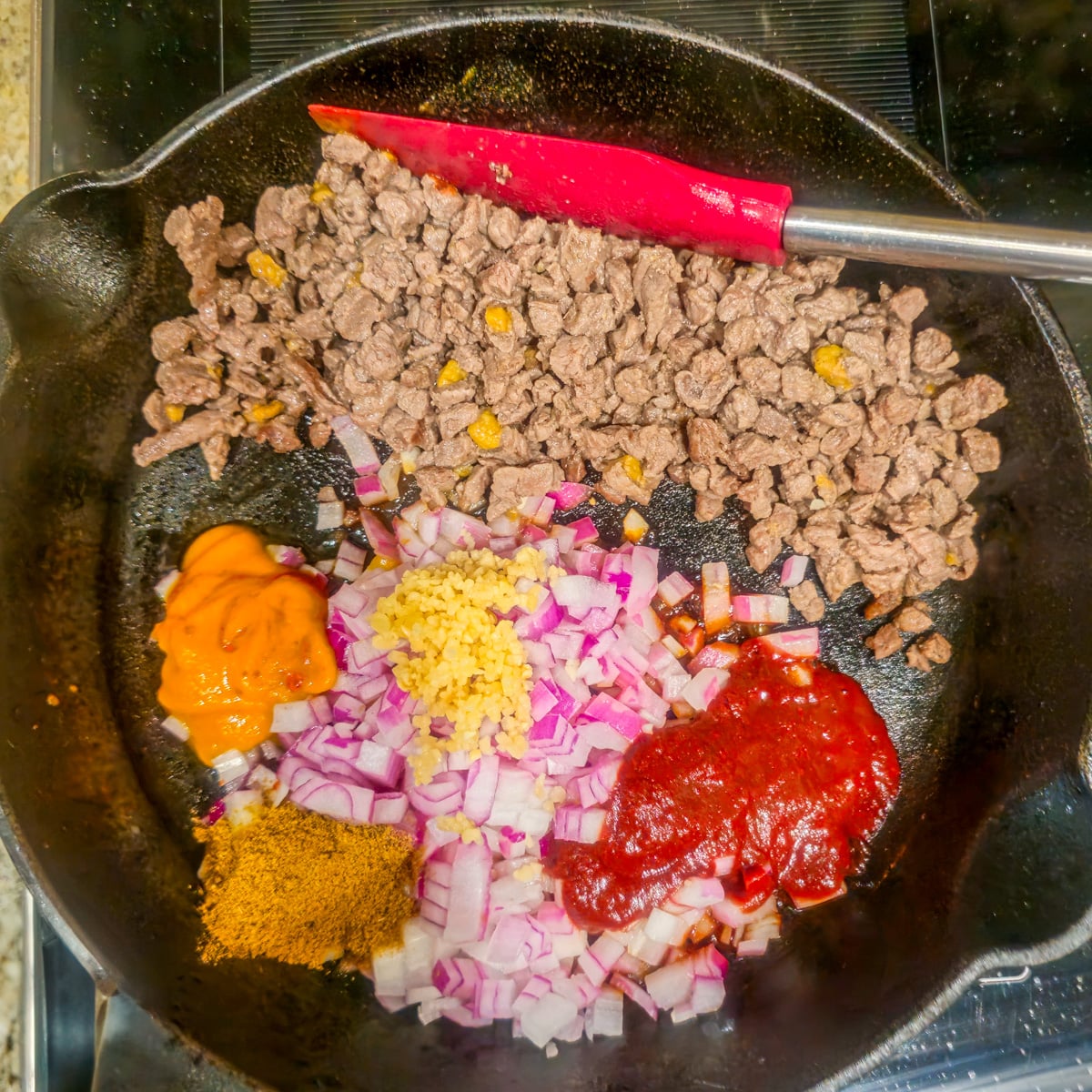 Step 2 - Browned bison is pushed aside and onions, garlic, pepper pastes, and spices are added to the skillet.