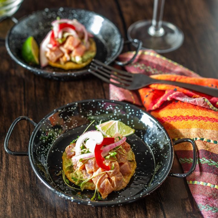 Two ahi tuna tostadas in mini paella pans with a colorful napkin and black fork.