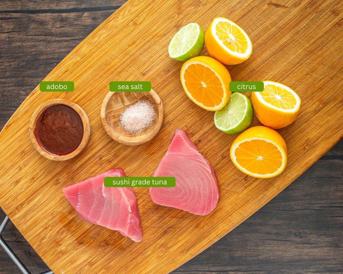 Ingredients for citrus-chipotle marinated tuna including citrus, chipotles, and sushi grade tuna on a wood cutting board.