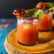 A live edge wood cutting board with to bloody mary cocktails with gin and taj&iacute;n.