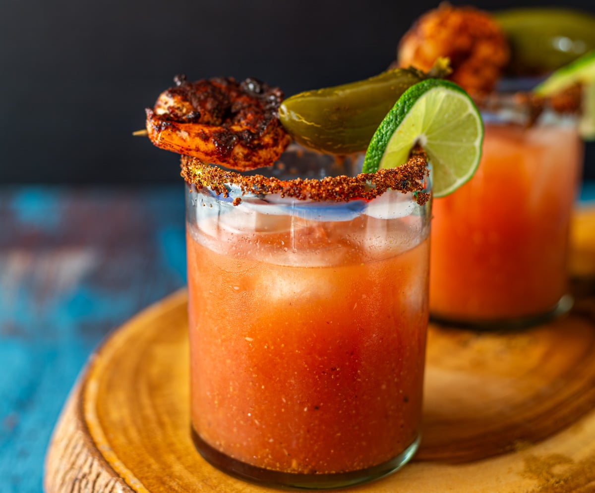 A close up of a Bloody Mary with Gin on a live edge wood cutting board.