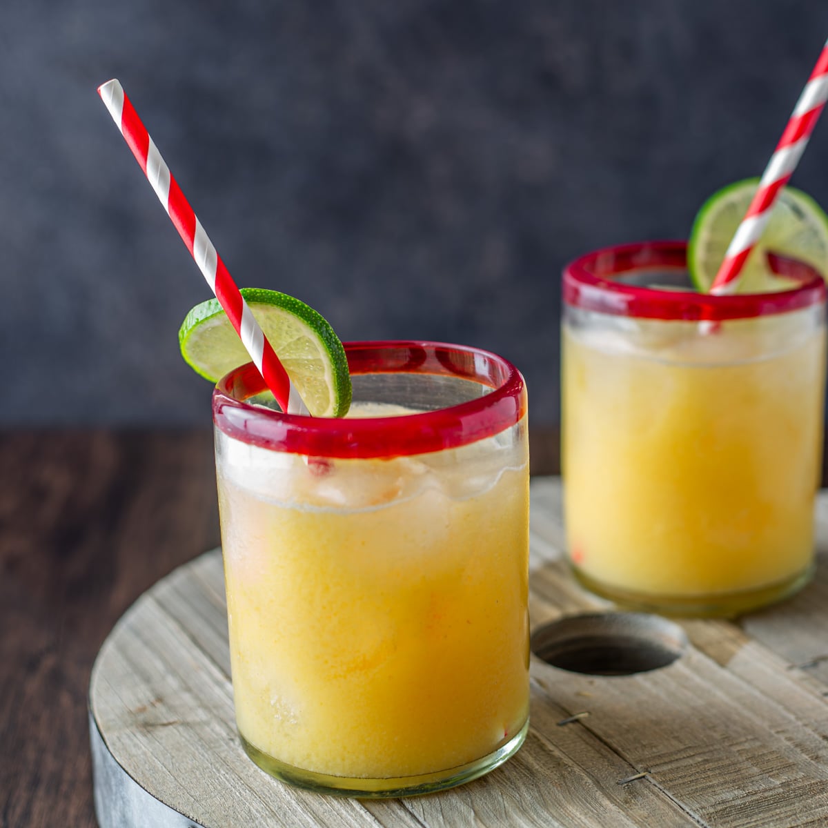 2 cachaca and passionfruit cocktails in red-rimmed rocks glasses with striped straws and lime wheels.