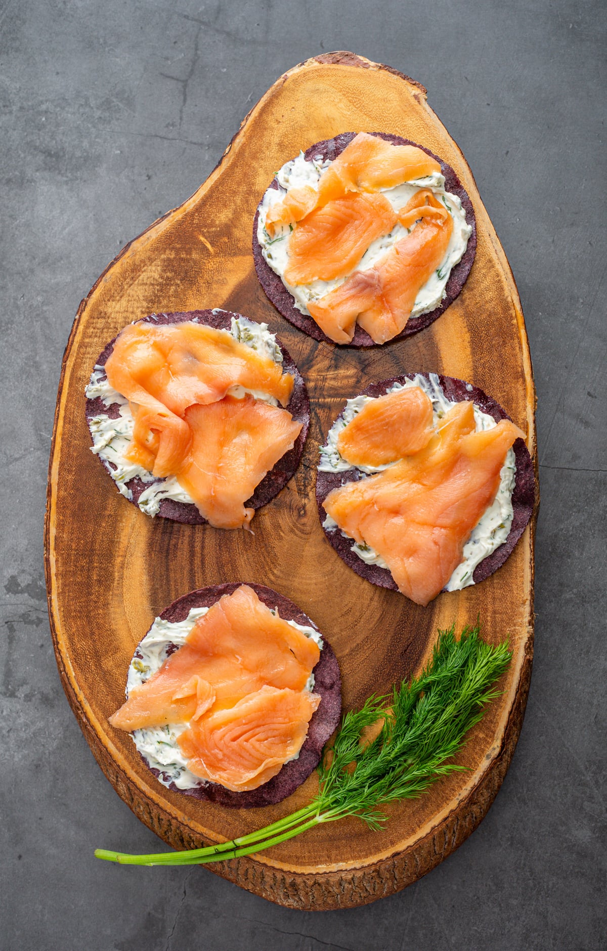 A wood cutting board with cream cheese layered on tostada shells with smoked salmon.