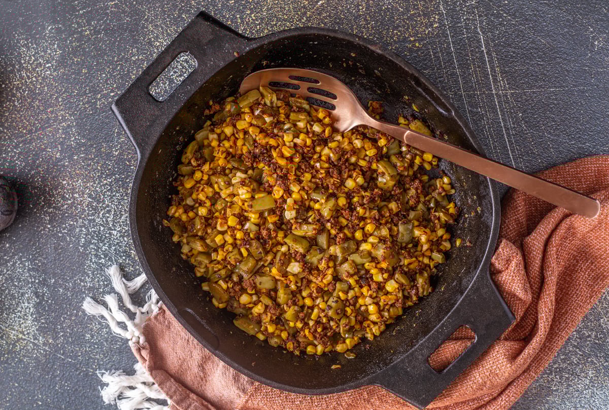 Step 4 - The charred corn, browned chorizo, and cooked nopalitos are combine in the skillet with copper spoon and cloth napkin.