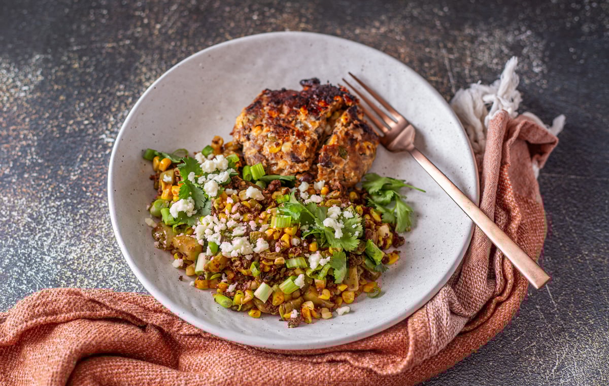A white ceramic bowl with the nopalitos with chorizo and a Mexican meatloaf patty.