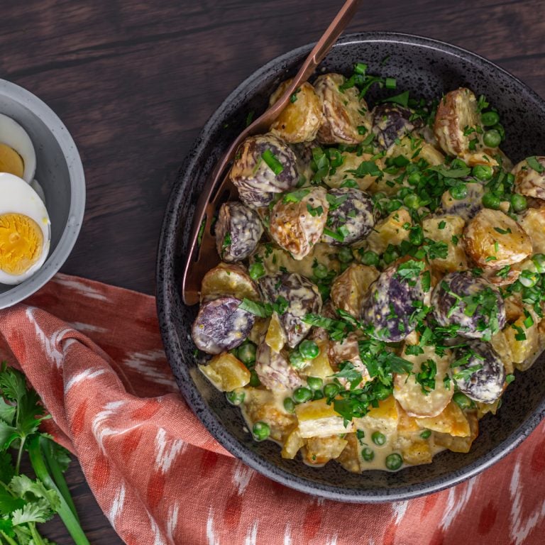 A black stoneware bowl with Peruvian potato salad with golden beets and peas.
