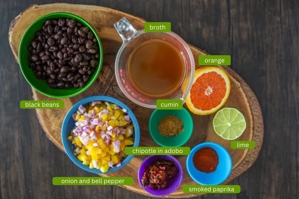 Ingredients for tropical buddha bowls including black beans, broth, citrus, spices, onion, and bell pepper.