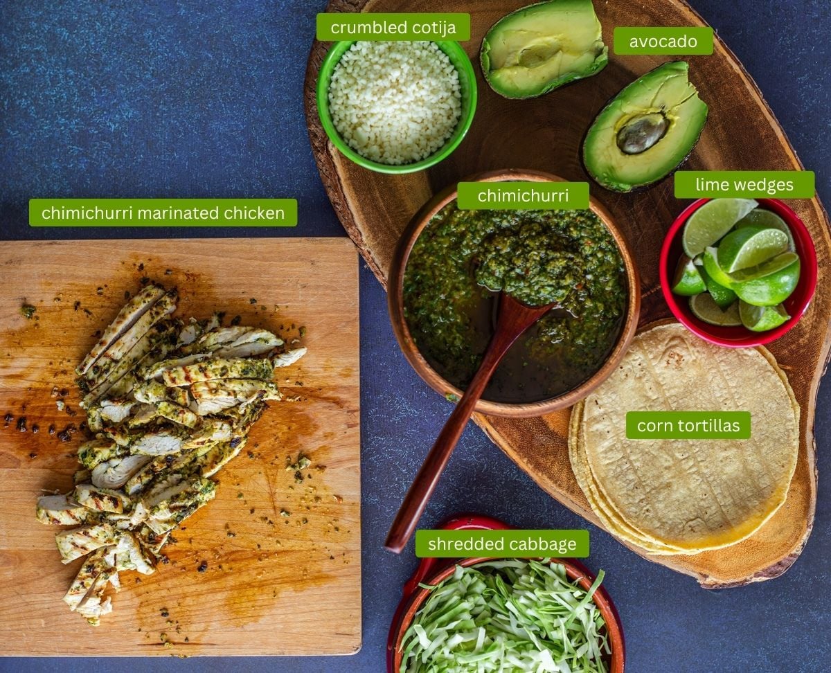 Chicken chimichurri tacos ingredients including chimichurri marinated chicken breast, corn tortillas, avocado, limes, and homemade cilantro chimichurri.