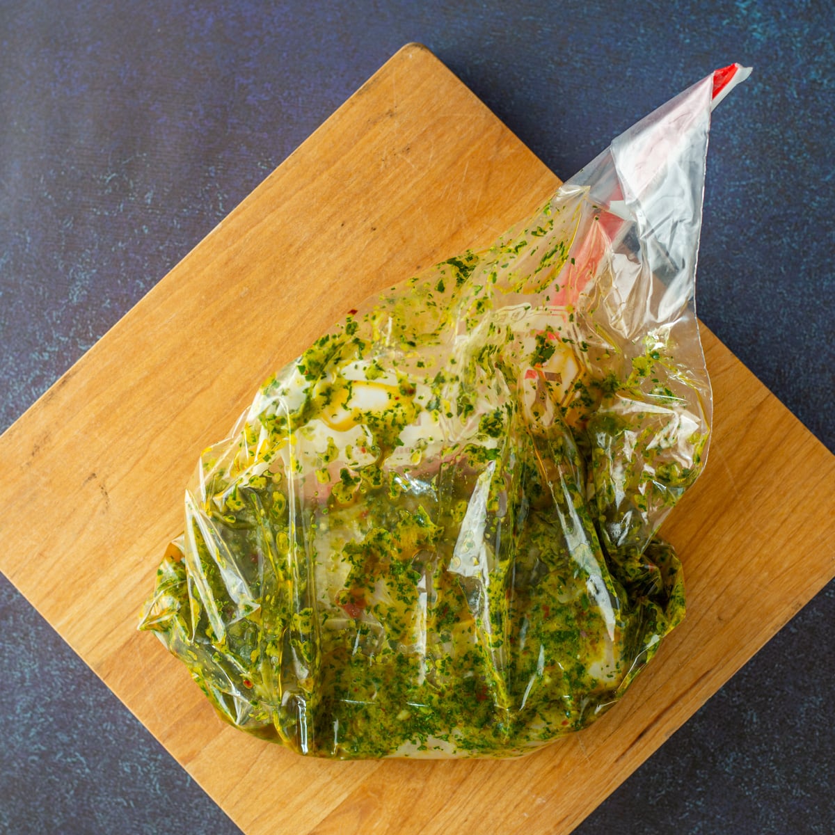 Thin-sliced chicken breast is marinated in cilantro chimichurri in a plastic bag.