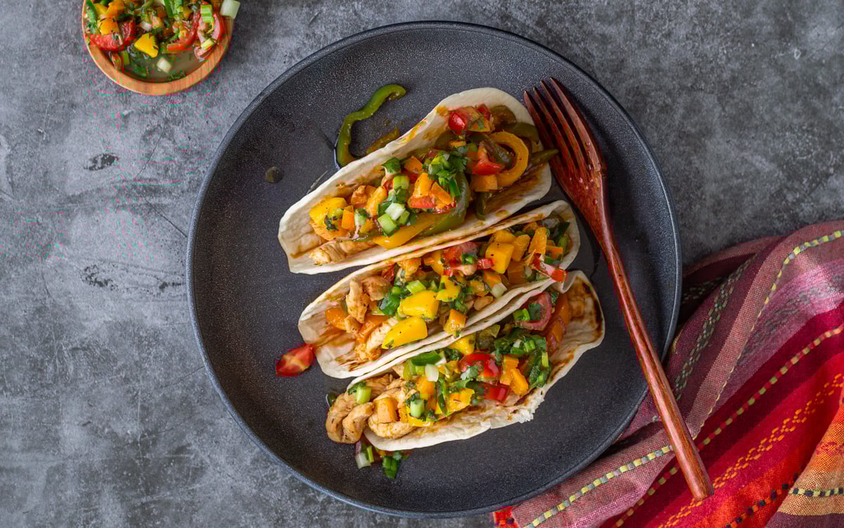 A bird's eye view of 3 Thai chicken curry tacos with wood fork and bright napkin.
