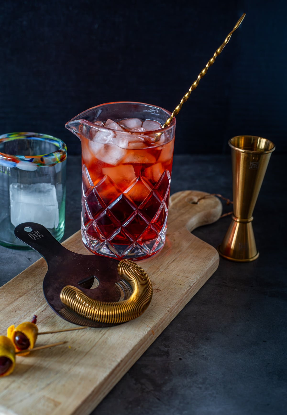 Mezcal, Campari, and sweet vermouth in a cocktail mixing glass with a copper stirring spoon.