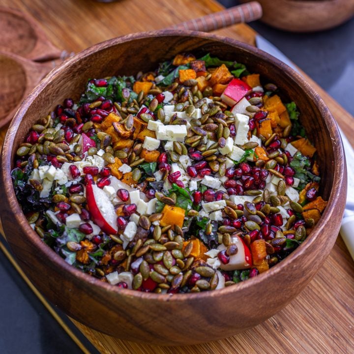 A wood salad bowl with Fall Kale Salad on a wood cutting board.