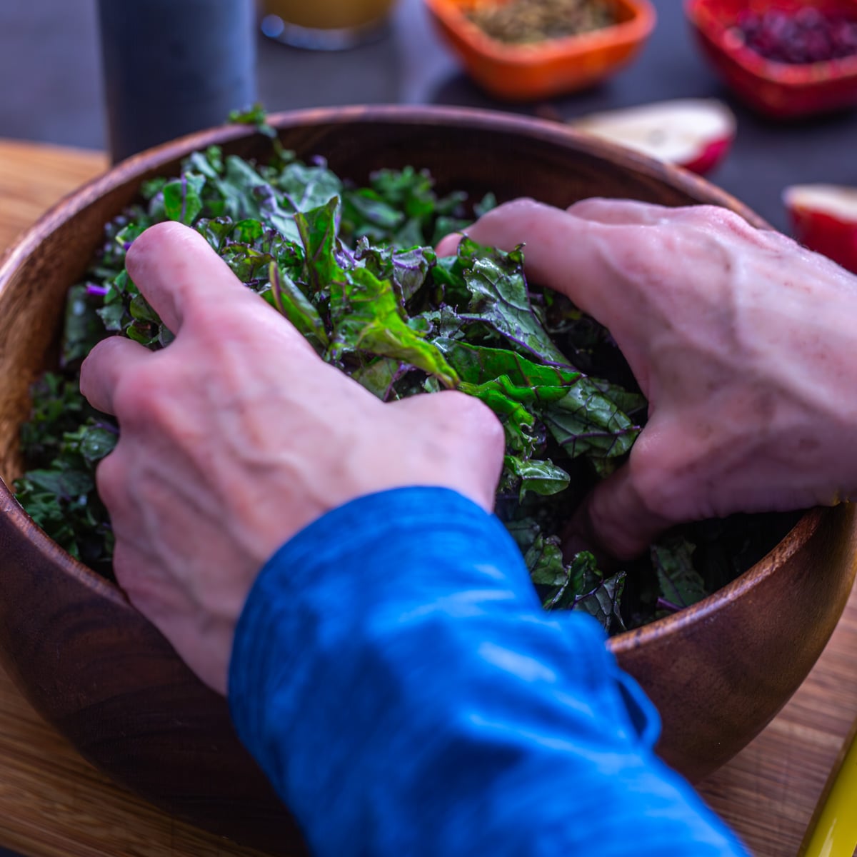 2 hands in the fresh purple kale massaging with fresh lemon juice in a wood salad bowl.