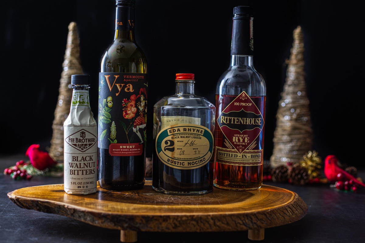 Ingredients for a black manhattan with nocino cocktail on a live edge wood board.