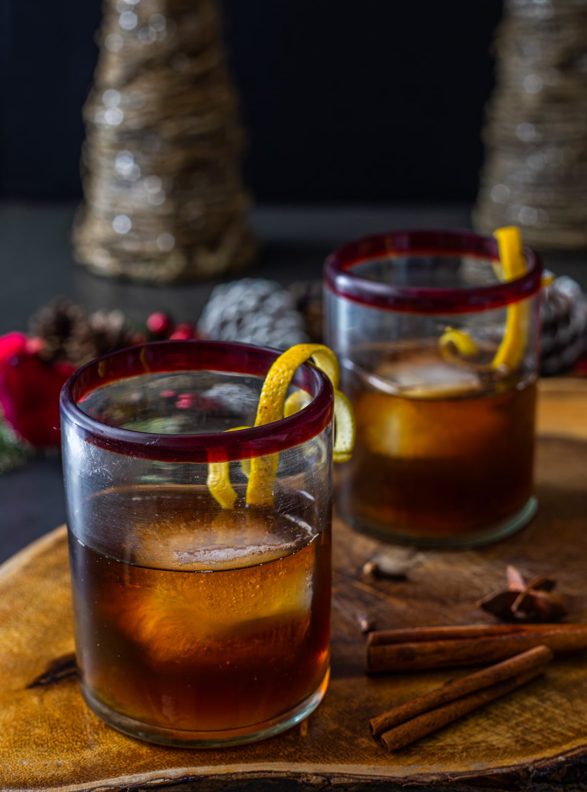 A wood board with 2 black manhattans with nocino along with whole spices.