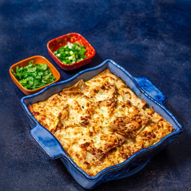 A blue ceramic baking dish with Christmas breakfast casserole, chopped scallions, and chopped cilantro.