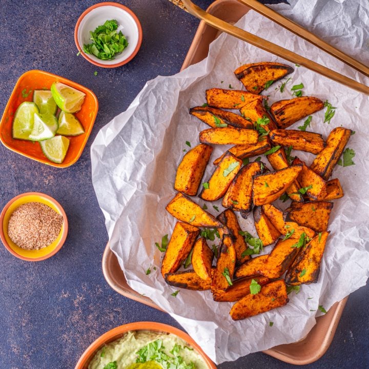A red ceramic bowl with sweet potato wedges coated with tajin spice mix.