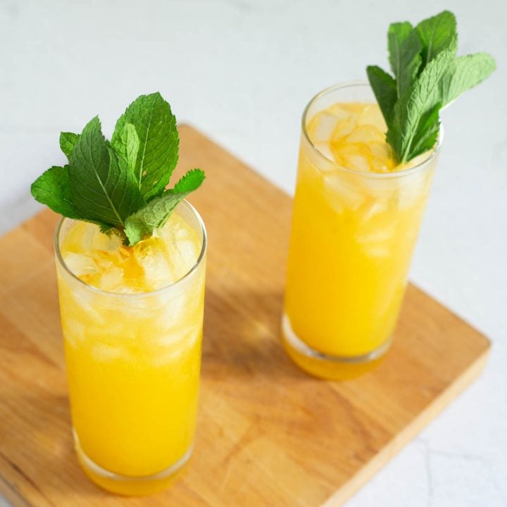 A wood cutting board with 2 chilcano cocktails garnished with mint sprigs.