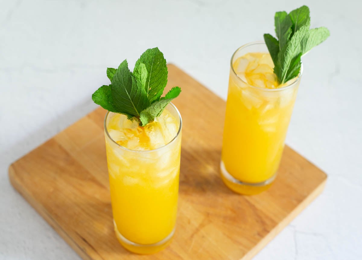 Chilcano de Maracuya in 2 glass highballs with mint sprigs on a green leaf platter with ice.