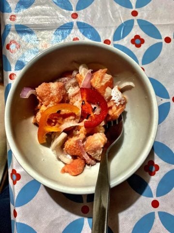 Ceviche de trucha in a white bowl on print table cloth.