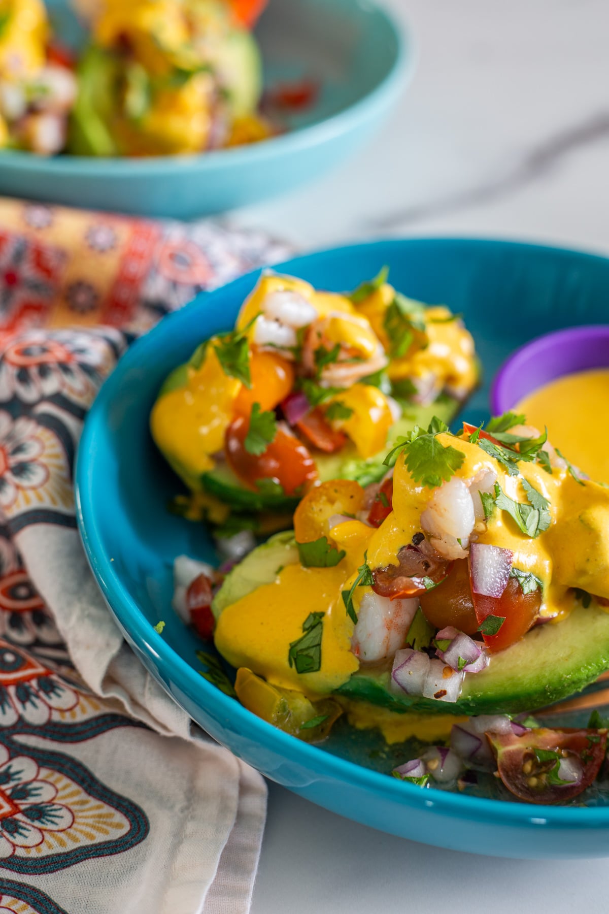 A close up of turquoise bowl with a palta rellena with shrimp and tomatoes.