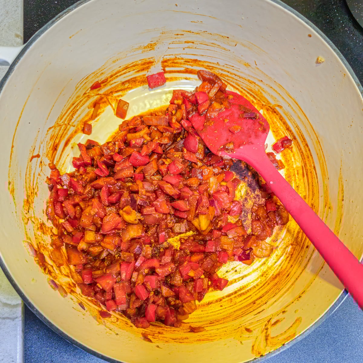 Aromatics are saut&eacute;ed in a white dutch oven with a red spatula.