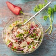 A close up a white ceramic bowl with Peruvian style redfish ceviche, air fryer sweet potato chips, canch, lime wedges, copper fork.