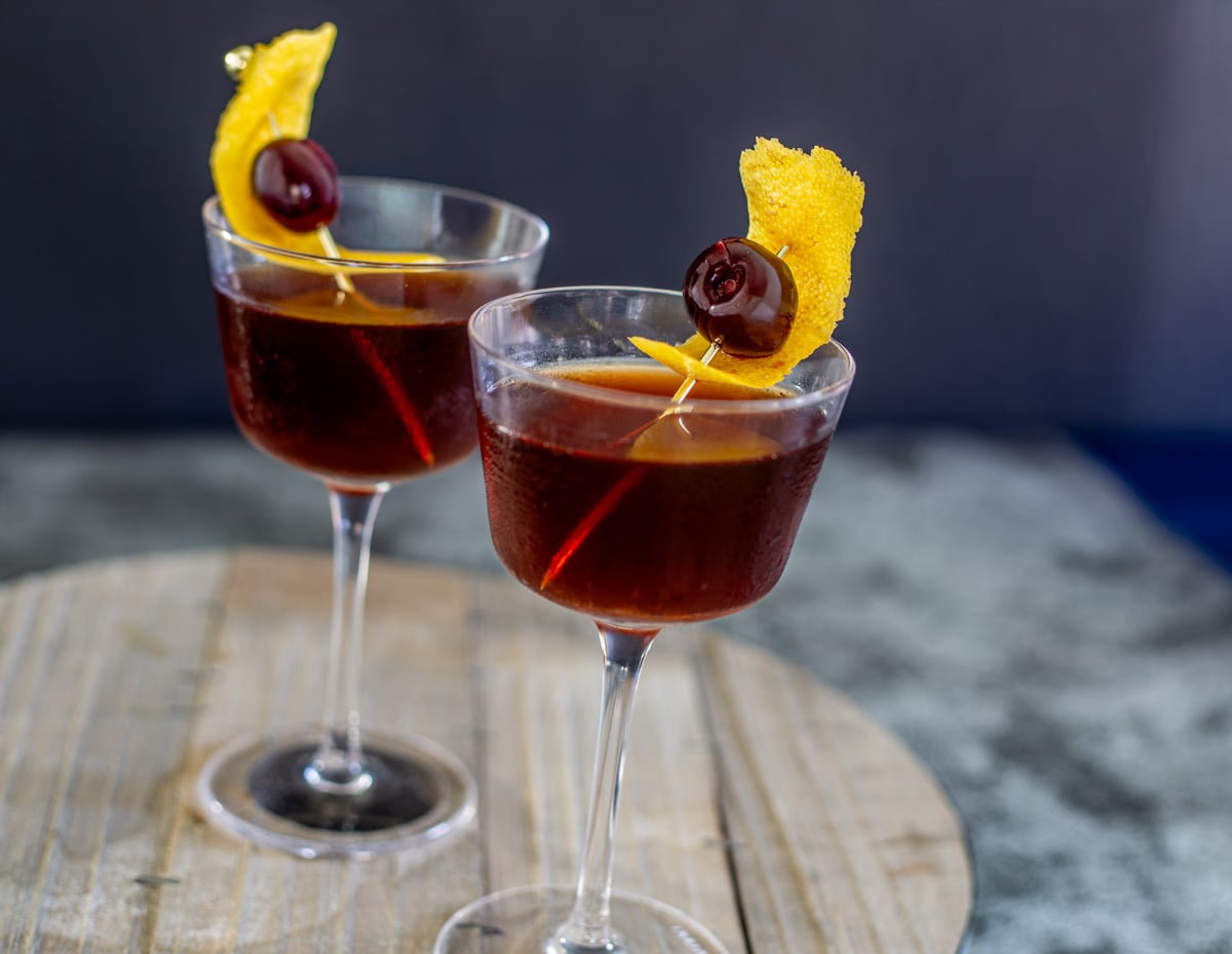 A round rustic wood tray with 2 nocino manhattan cocktails.