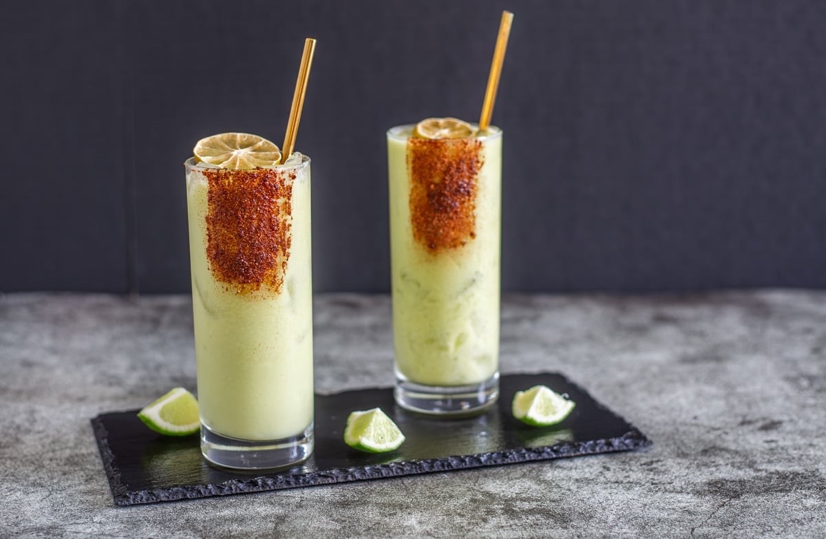 Two mezcal margaritas on a slate tray with gold straws.