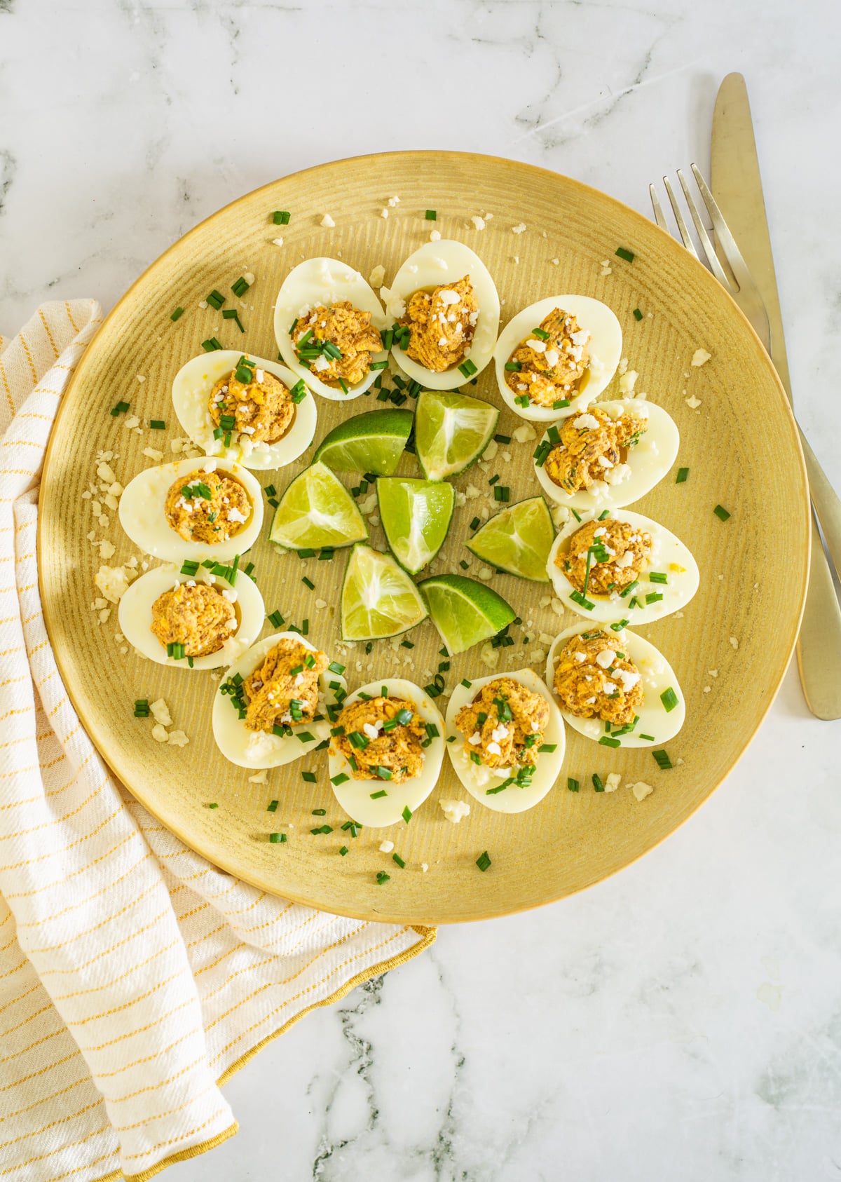 A yellow plate with a dozen Mexican deviled eggs on a marble background with cloth napkin.