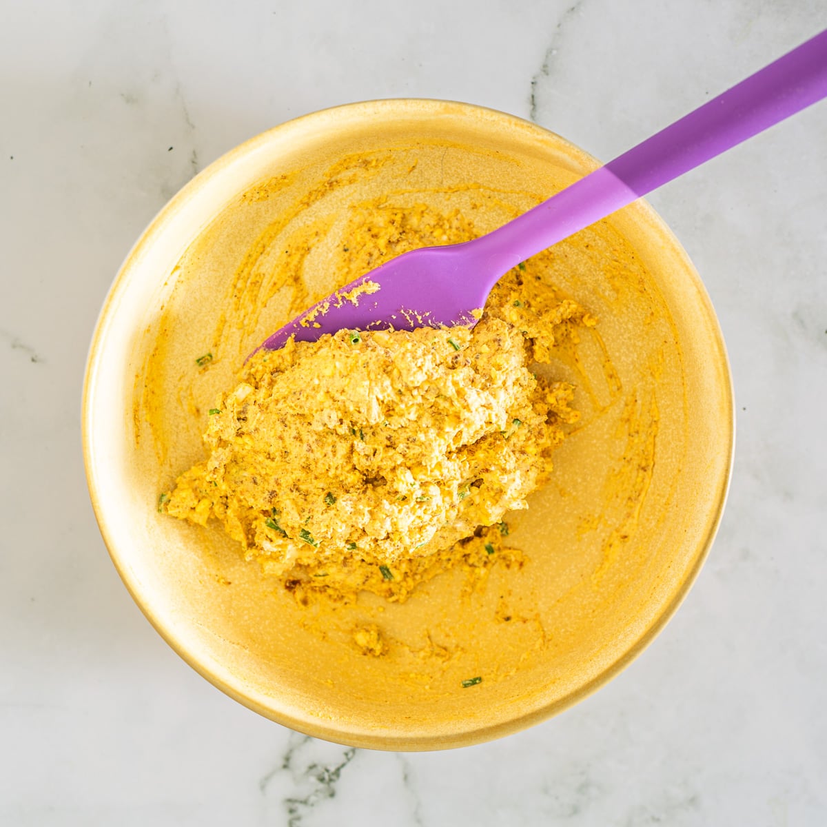 The egg yolk, chorizo, and other ingredients are combined in a yellow ceramic bowl.