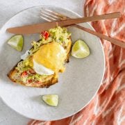 A white ceramic plate with Peruvian eggs benedict and copper flatware and print napkin.