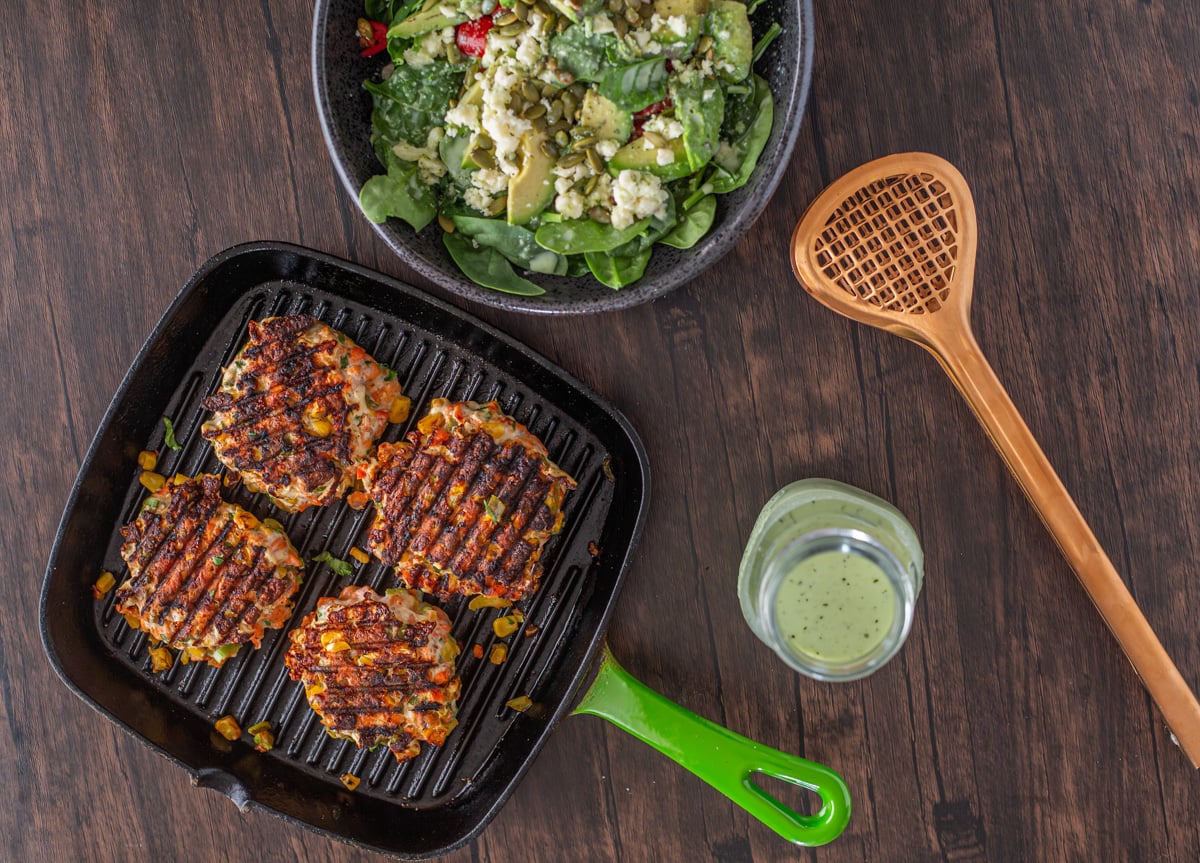 A griddle pan with 4 salmon patties, a spinach salad, and a jar of cilantro jalape&ntilde;o ranch dressing.