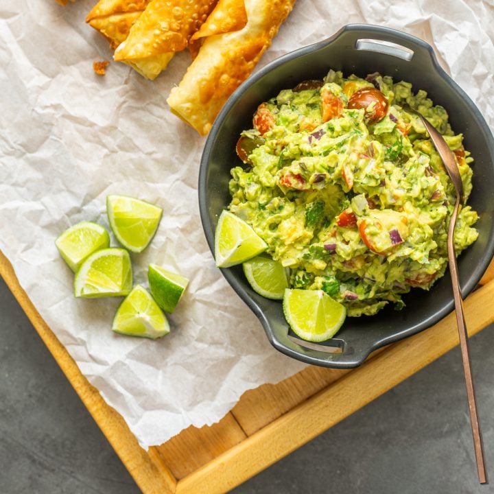 A black ceramic bowl of salsa de palta on parchment with teque&ntilde;os.