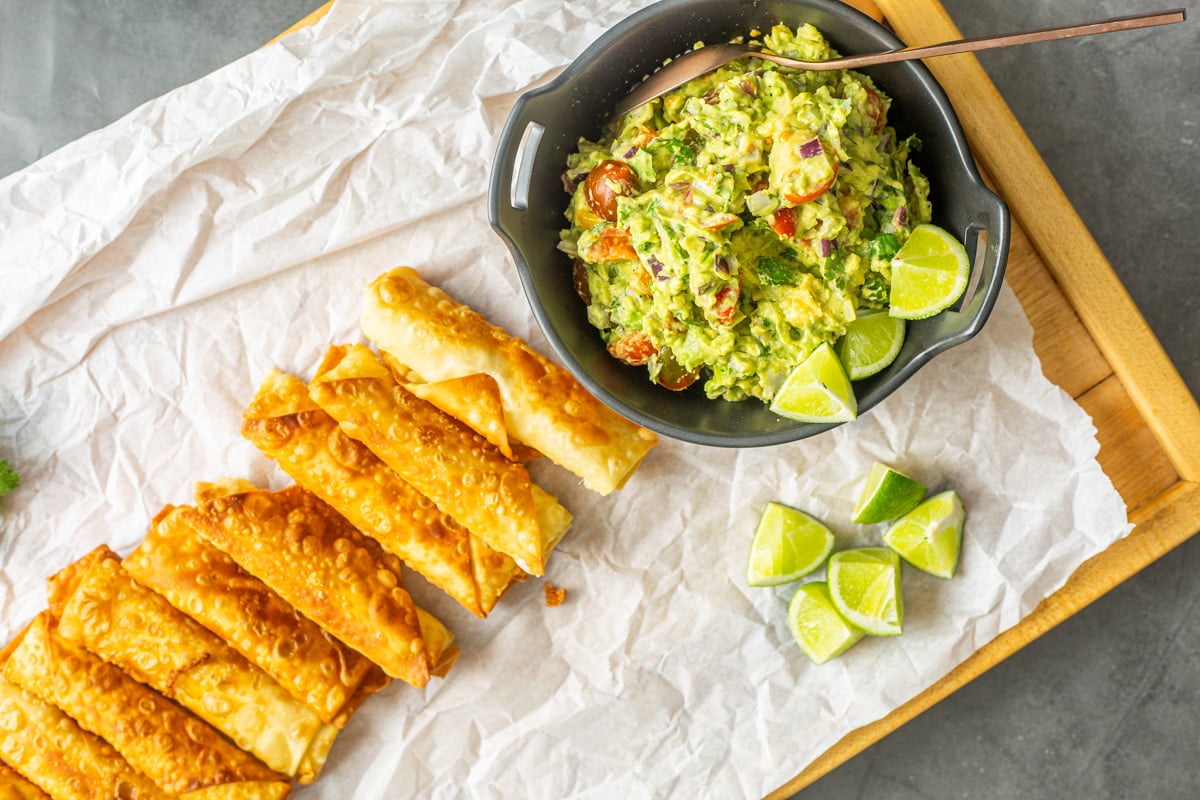 A wood tray with Peruvian teque&ntilde;os and guacamole in a black bowl.