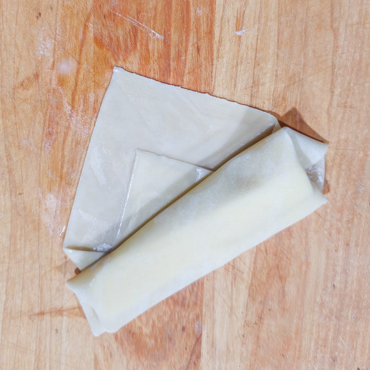 A partially wrapped and rolled cheese tequeno on a cutting board.