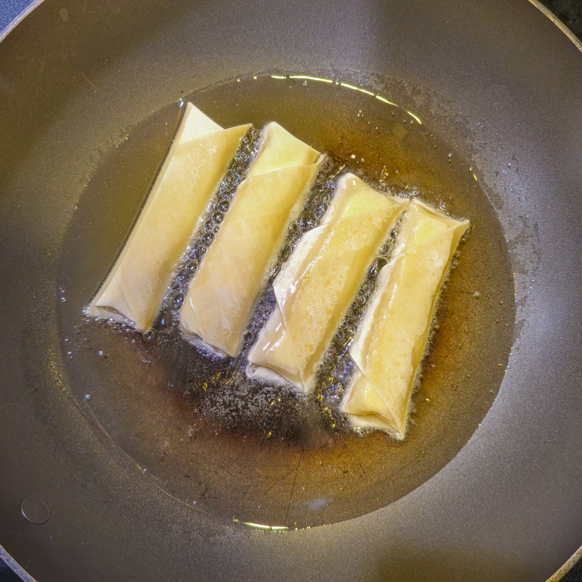 4 tequenos in oil in a fry pan.