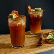 2 miso micheladas with bacon, shrimp, and lime garnish in pub glasses.