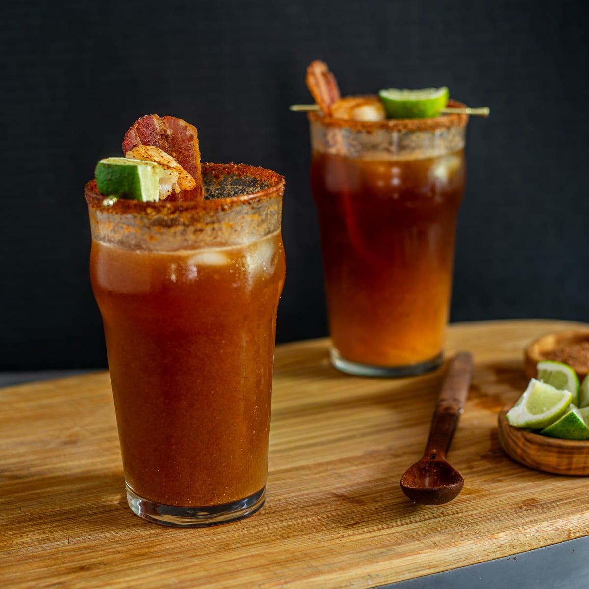 2 miso micheladas with bacon, shrimp, and lime garnish in pub glasses.