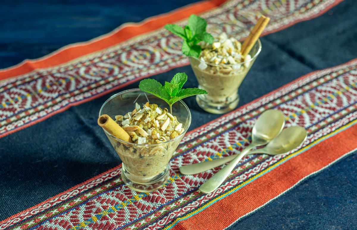 2 spoons with 2 portions of quinoa con leche garnished with almonds and toasted coconut along with mint sprig and cinnamon stick.